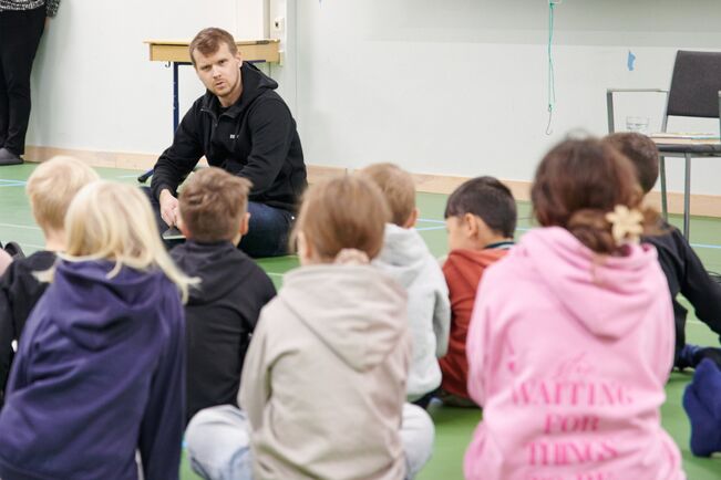 Kaupunginjohtaja Eero Vainio lukulähettiläänä Kaanaan koulussa. Kuulijana kuudesluokkalaisia. Kirjana Tove Janssonin Vaarallinen juhannus.