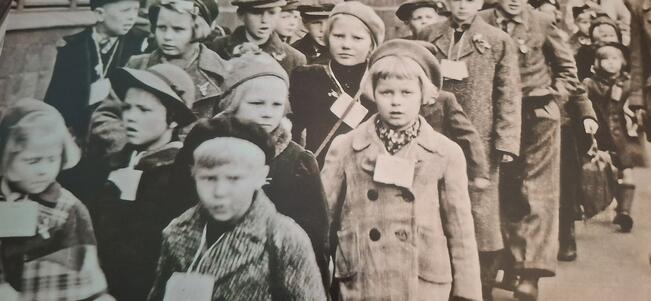 Kuvassa kameraan tuijottaa 7-vuotias tyttö, joka odottaa sijaisvanhempia juna-asemalla Ruotsissa jatkosodan aikana. Tällä hetkellä tyttö on melkein 90-vuotias, ja hänen elämässään on tapahtunut valtavasti tuon valokuvan ottamisen jälkeen.